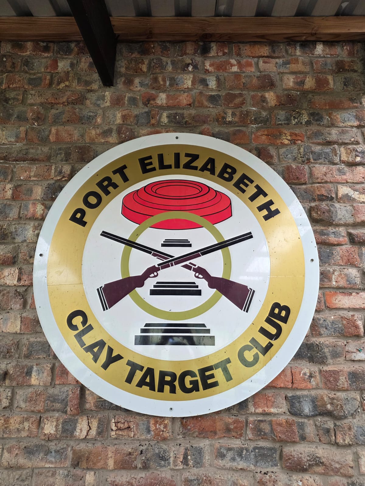 The painted Port Elizabeth Clay Target Club badge mounted on the clubhouse brick wall
