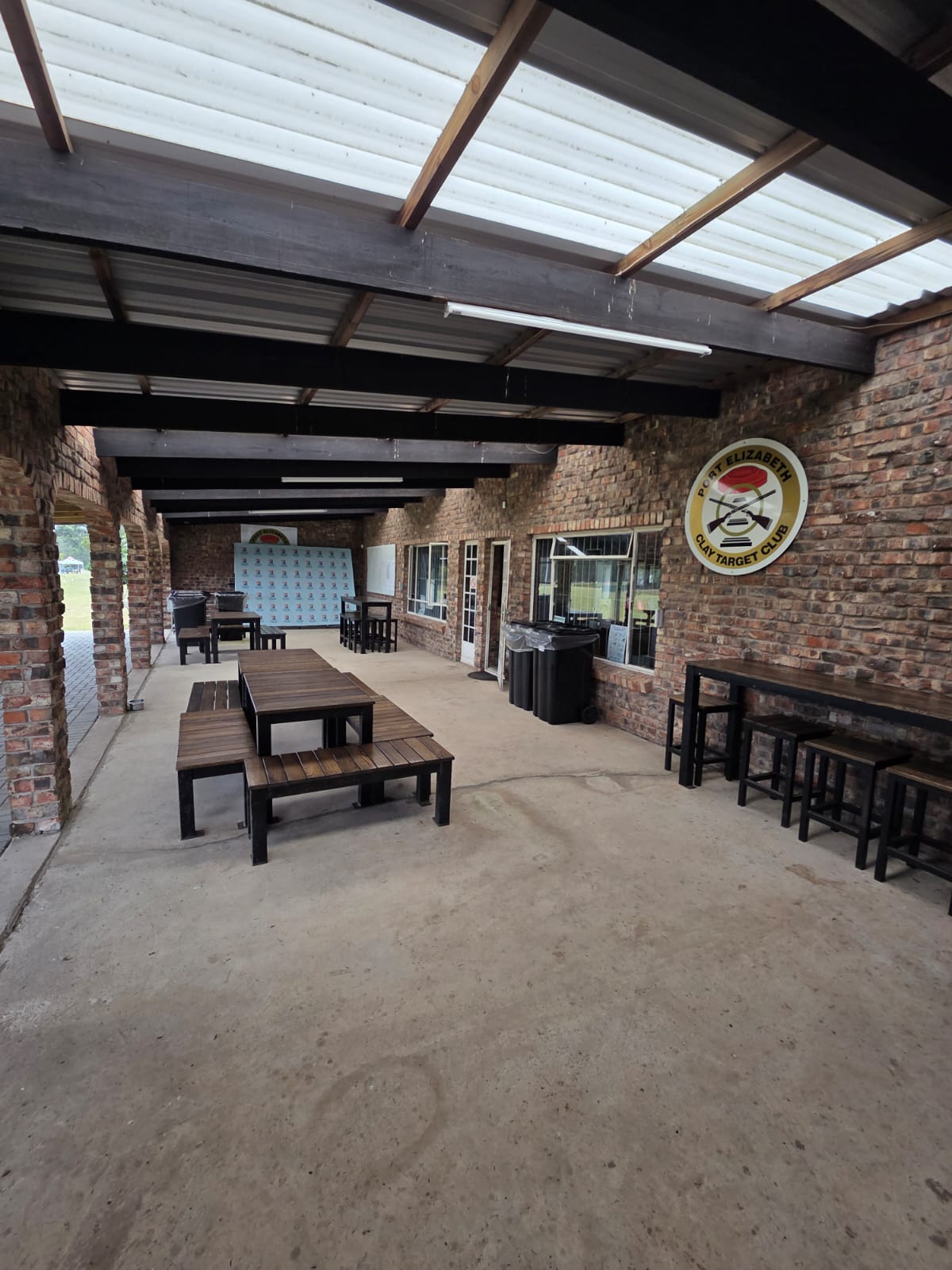 The covered brick patio at PECTC with picnic tables, the club badge and sponsor boards on the wall