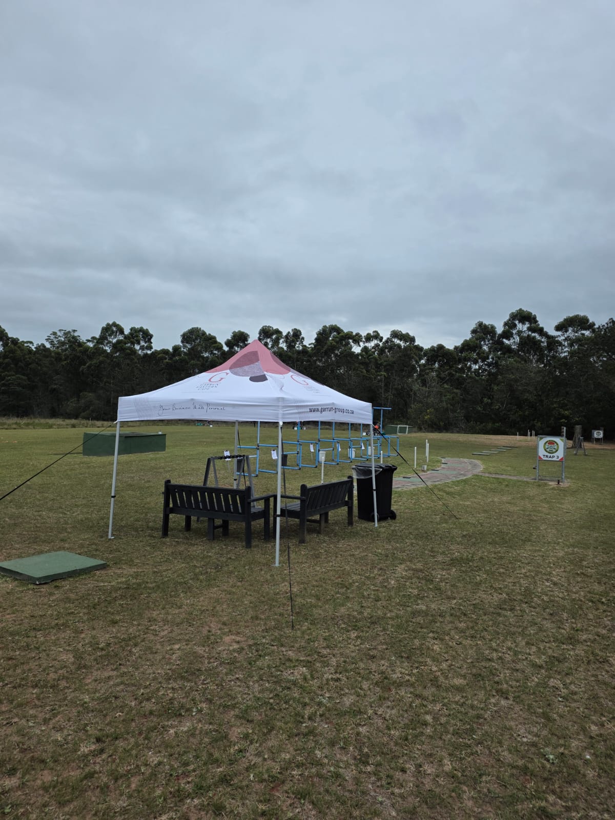 A branded gazebo, bench and gun rack beside the Trap 3 sign on the grass range at PECTC