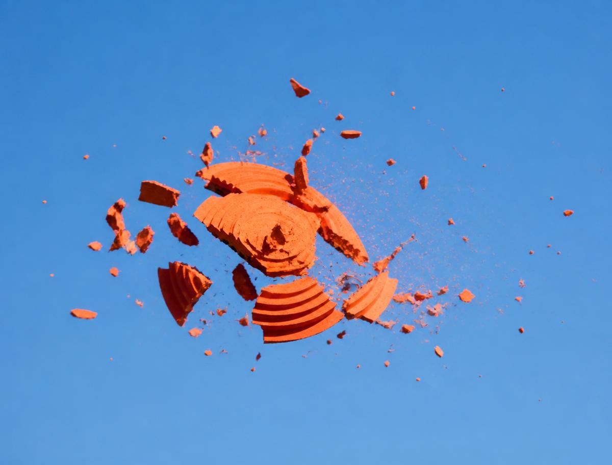 An orange clay target breaking apart against a blue sky